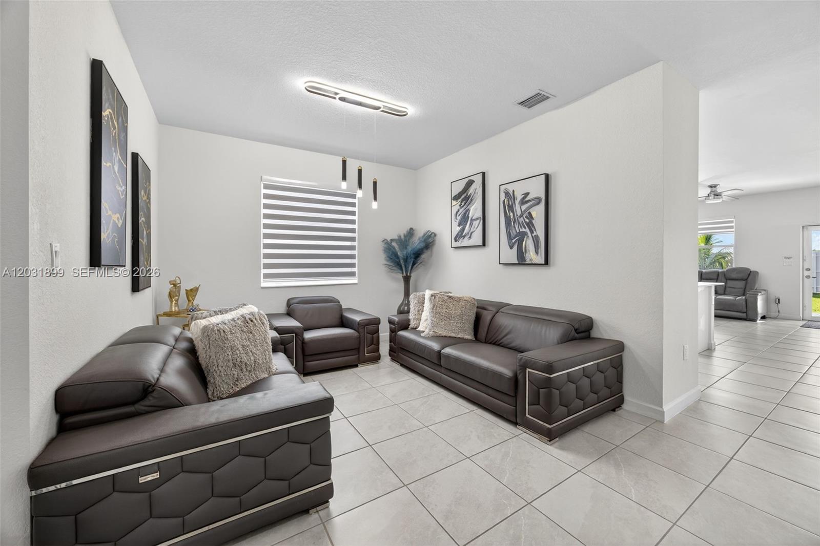 A living room features dark leather furniture, tiled floors, and abstract wall art — 21363 SW 127th Ct, Miami FL 33177, MIAMI, FL
