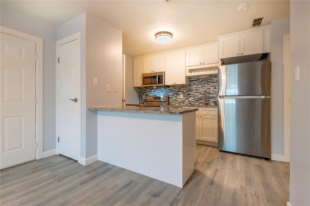 A kitchen features white cabinets, stainless steel appliances, a granite countertop, and gray wood flooring — 1400 GANDY BOULEVARD N UNIT 1010, ST PETERSBURG, FL