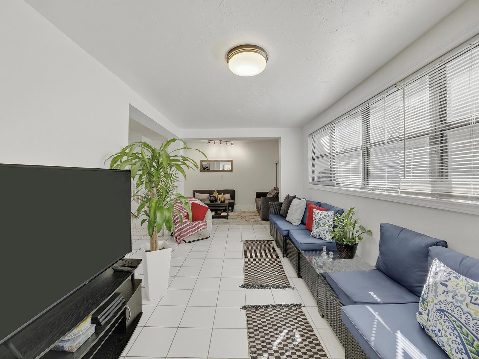 A long living room features white tile floors, a large television, and blue patio furniture — 9702 NW 5th Lane # 9702, Miami FL 33172, MIAMI, FL