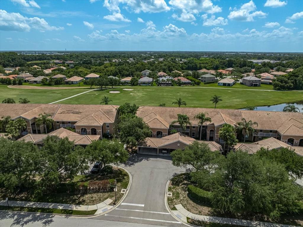 An aerial view shows a multi-unit residential building overlooking a golf course and pond — 915 FAIRWAYCOVE LANE UNIT 201, BRADENTON, FL