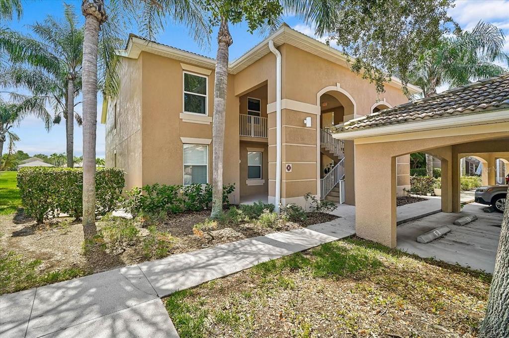 A two-story tan stucco apartment building features a covered parking area and outdoor stairs — 915 FAIRWAYCOVE LANE UNIT 201, BRADENTON, FL