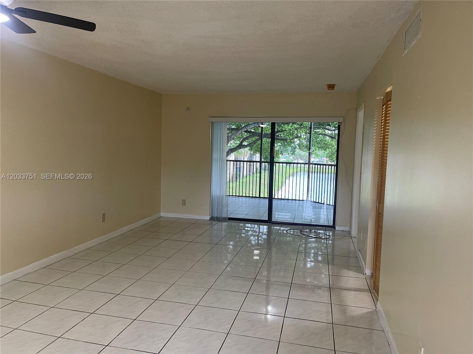 An empty living room features light-colored tile flooring, beige walls, and a sliding glass door — 3252 Foxcroft Rd # 307, Miramar FL 33025, MIRAMAR, FL