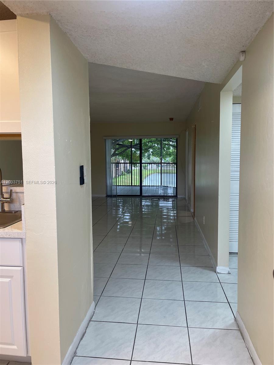 A tiled hallway leads from a kitchen toward a living area with sliding glass doors — 3252 Foxcroft Rd # 307, Miramar FL 33025, MIRAMAR, FL