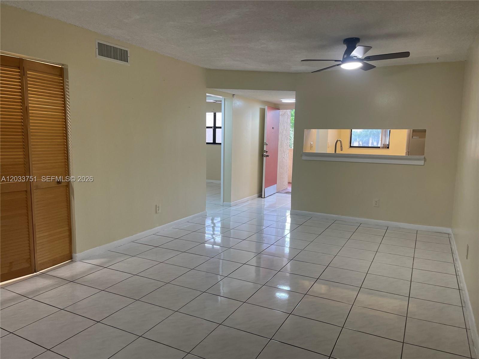 An empty room with white tile flooring, a ceiling fan, and a kitchen pass-through window — 3252 Foxcroft Rd # 307, Miramar FL 33025, MIRAMAR, FL