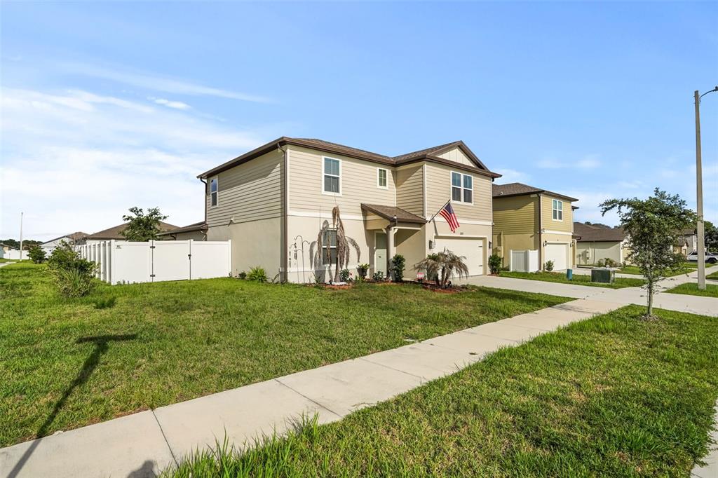 A two-story suburban house with beige siding and a white fence on a sunny day — 1217 MICHELANGELO LANE, WINTER HAVEN, FL