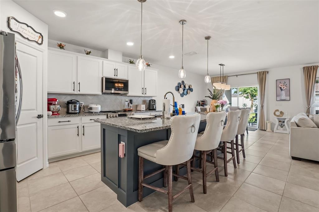 A kitchen with a dark blue island, white cabinets, granite countertops, and bar stool seating — 1217 MICHELANGELO LANE, WINTER HAVEN, FL