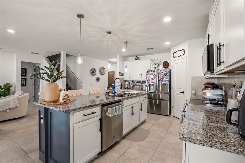 A kitchen with white cabinets, a dark blue island, granite countertops, and stainless steel appliances — 1217 MICHELANGELO LANE, WINTER HAVEN, FL