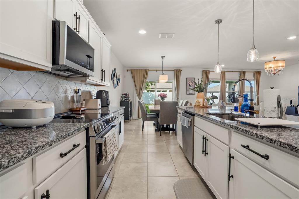 A modern kitchen with white cabinets, granite countertops, and stainless steel appliances overlooks a dining area — 1217 MICHELANGELO LANE, WINTER HAVEN, FL