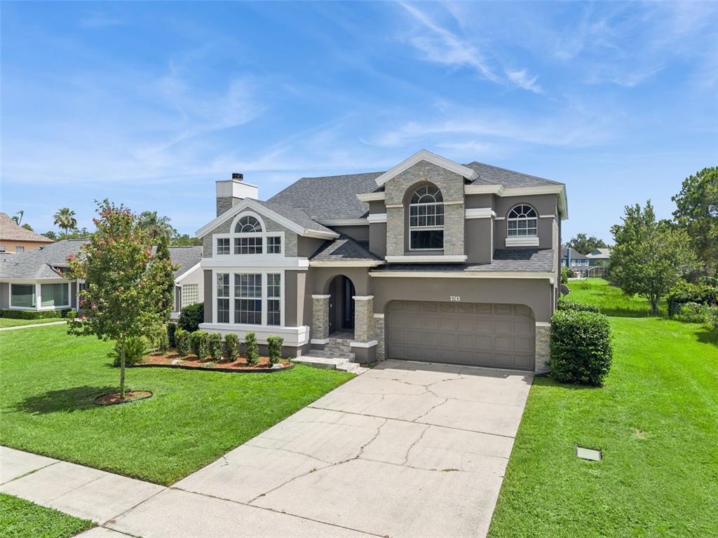 A two-story suburban house with a gray stucco exterior, stone accents, and a two-car garage — 2743 RUNNING SPRINGS LOOP, OVIEDO, FL