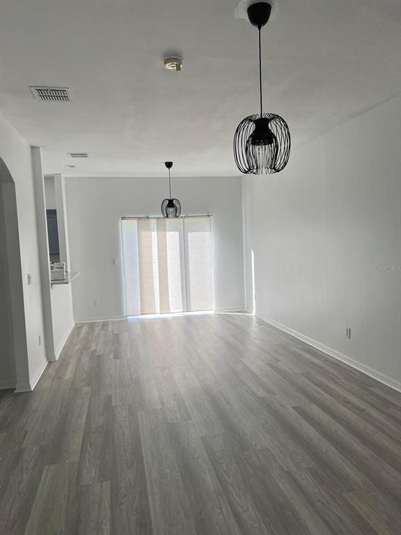 An empty living room features light gray wood-look flooring, white walls, and two pendant lights — 4344 PARADISE COVE COURT, KISSIMMEE, FL