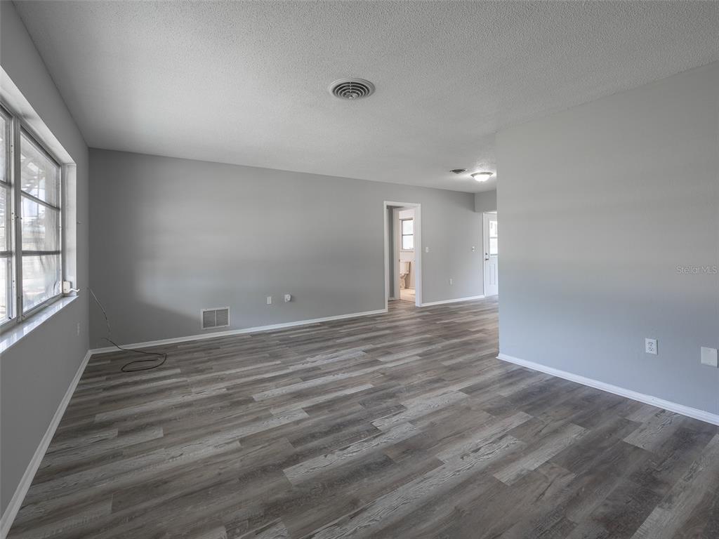 An empty room features gray walls, wood-look vinyl flooring, and a large window with shutters — 916 GILLESPIE STREET, ENGLEWOOD, FL