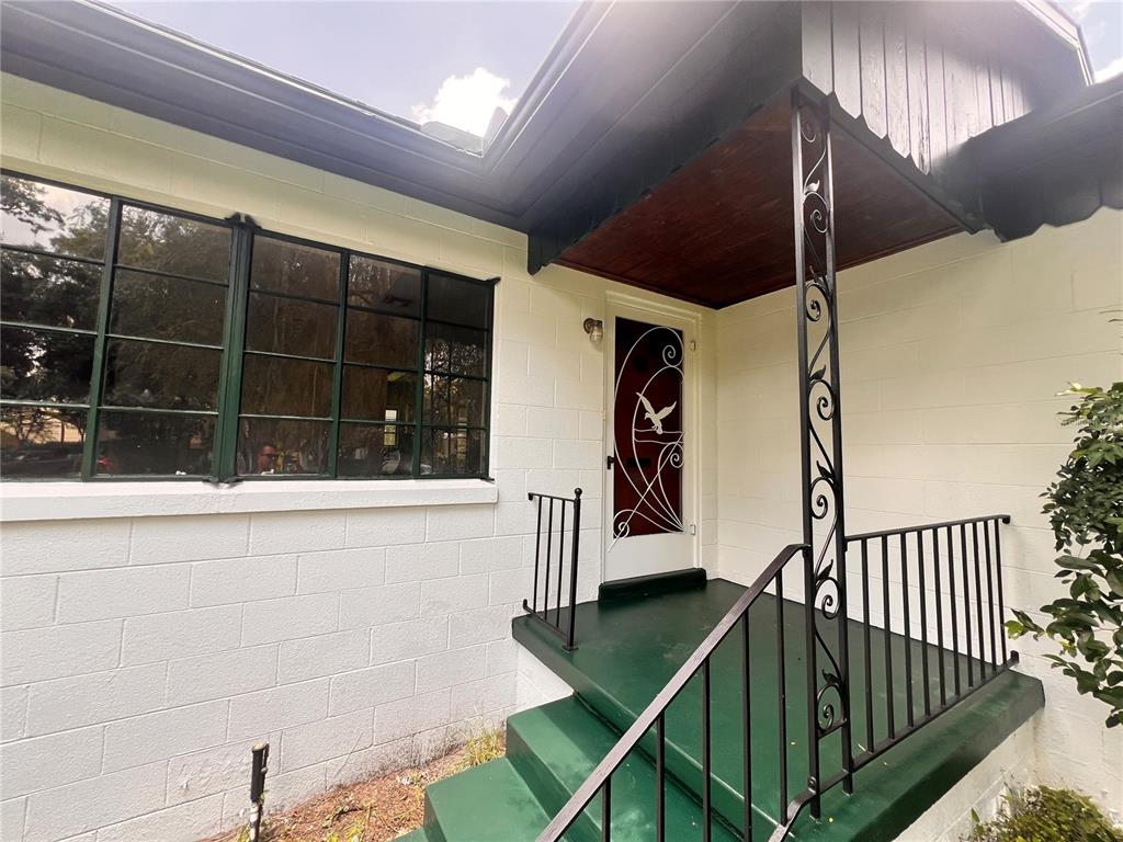 A white concrete block house exterior features a green porch, stairs, and a decorative screen door — 1261 RICHMOND ROAD, WINTER PARK, FL