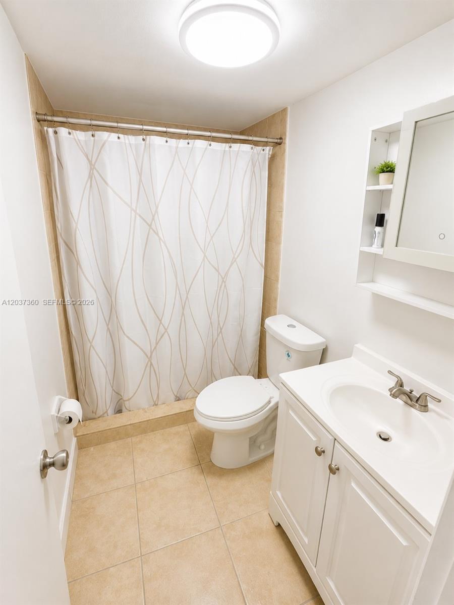 A small bathroom features a white vanity, a toilet, and a shower with a patterned curtain — 8650 SW 109th Ave # 103, Miami FL 33173, MIAMI, FL
