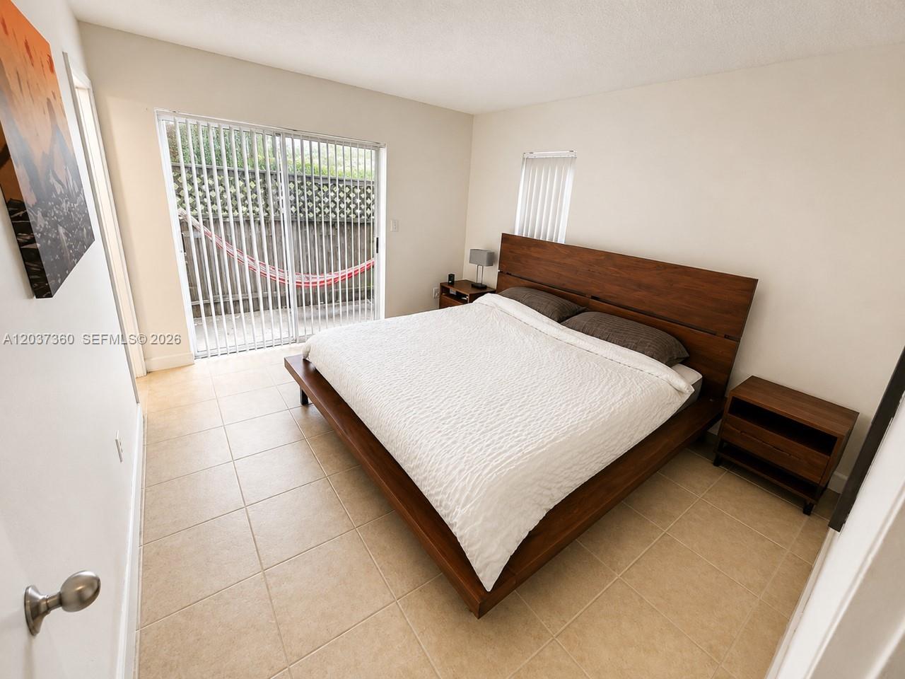 A bedroom features a wooden platform bed, tile flooring, and a sliding glass door — 8650 SW 109th Ave # 103, Miami FL 33173, MIAMI, FL
