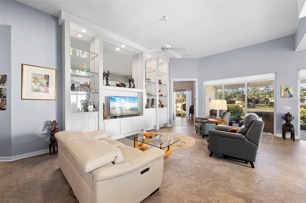 A living room features a large white built-in entertainment center, tile flooring, and sliding glass doors — 5735 WILENA PLACE, SARASOTA, FL