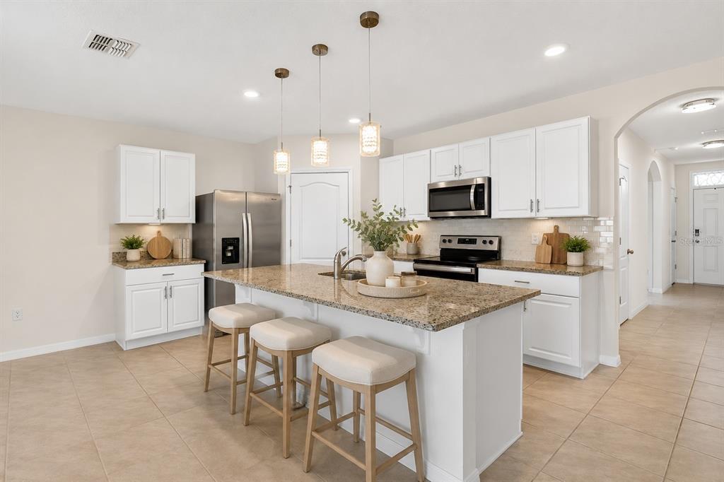 A kitchen features white cabinets, granite countertops, a center island with stools, and stainless appliances — 1673 BARBERRY DRIVE, KISSIMMEE, FL