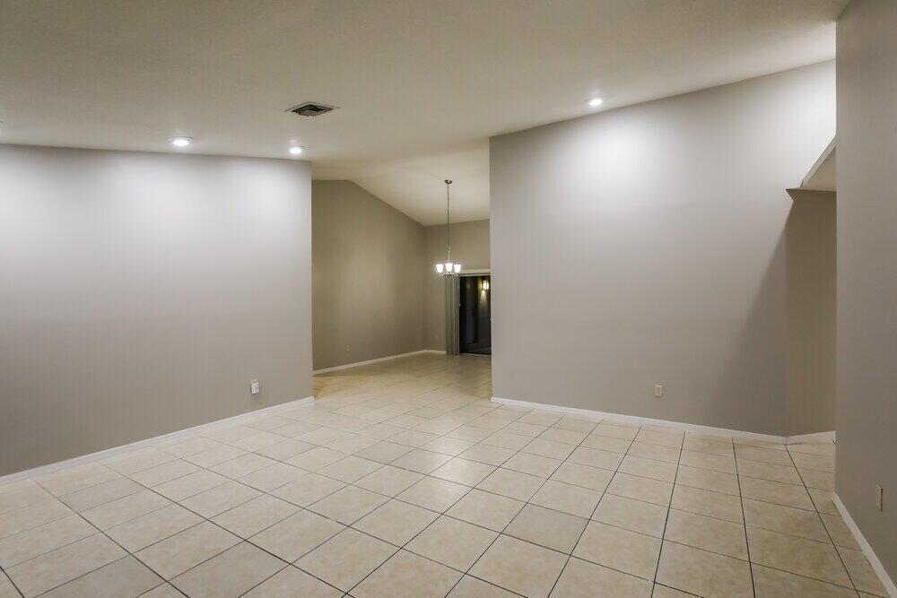 An empty room with beige tile flooring, light gray walls, and a vaulted ceiling — HOMESTEAD, FL