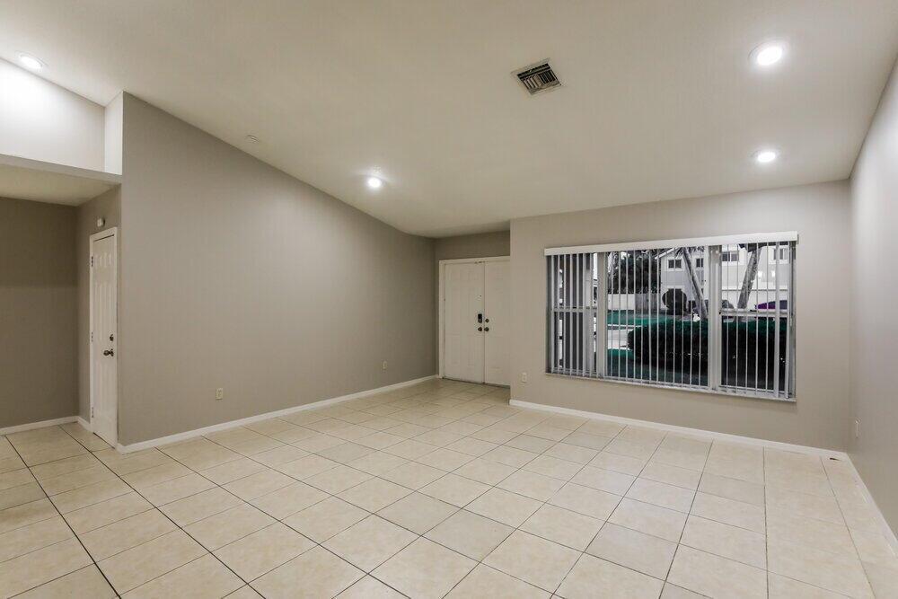 An empty living room with light-colored tile flooring, gray walls, and a large window — HOMESTEAD, FL