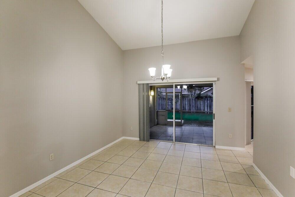 A dining room with beige tile floors, a vaulted ceiling, and a sliding glass door — HOMESTEAD, FL
