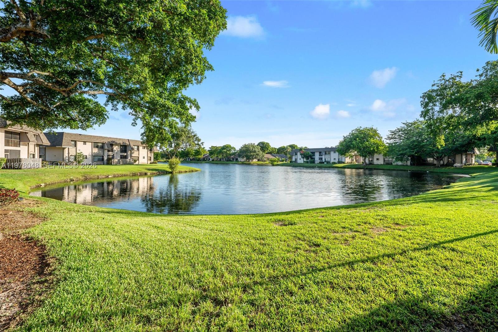 A grassy lawn slopes down to a pond surrounded by multi-story apartment buildings and trees — 3631 NW 94th Ave # 6G, Sunrise FL 33351, SUNRISE, FL