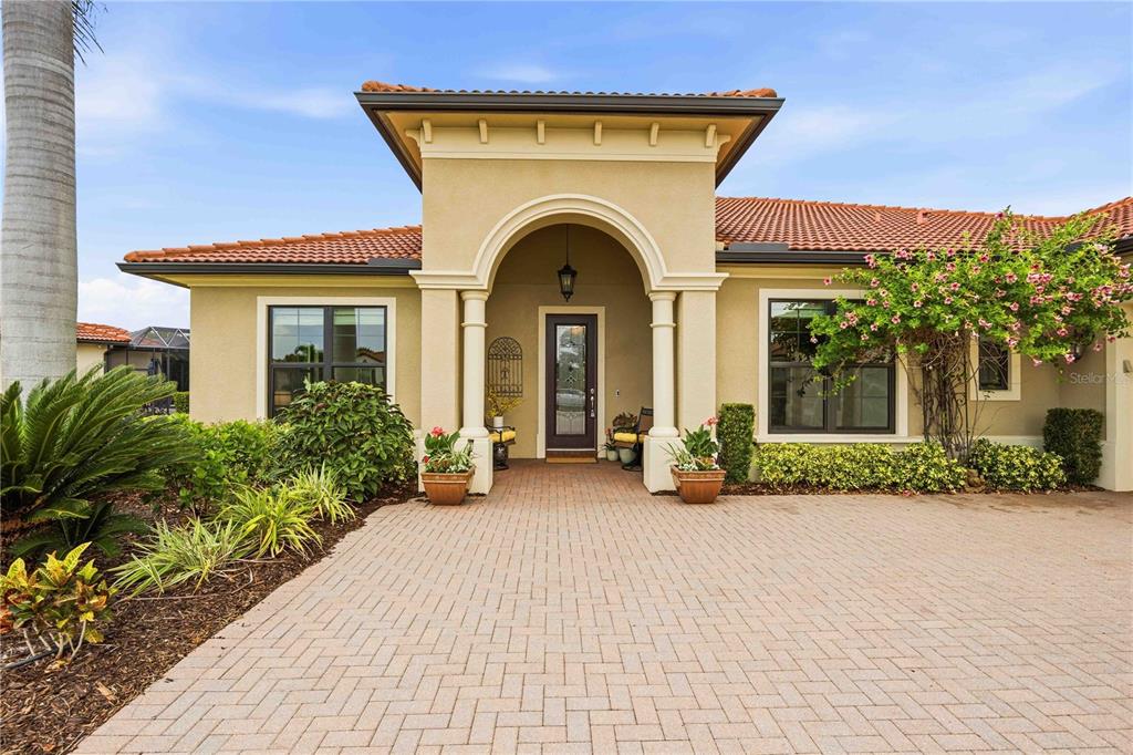 A paved driveway leads to the arched entryway of a tan stucco house with tile roofing — 10944 BULLRUSH DRIVE, VENICE, FL