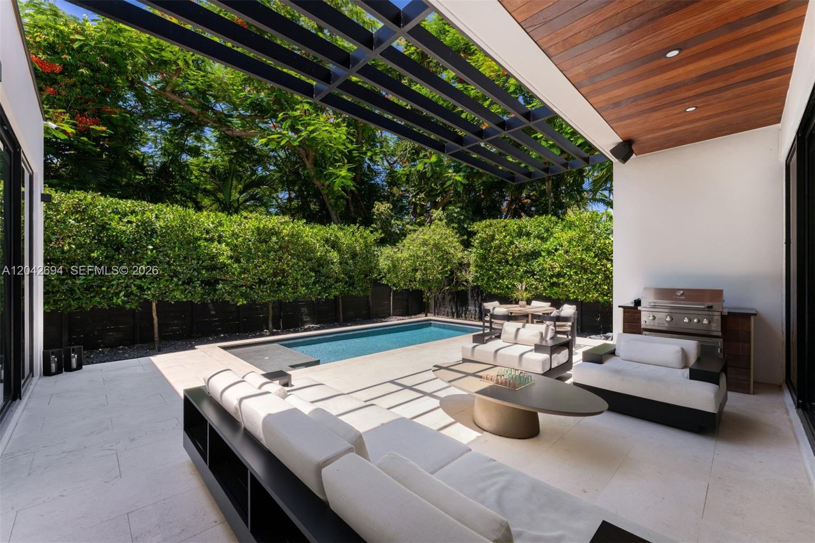 A modern outdoor patio features a swimming pool, lounge seating, and a built-in grill area — 661 NE 120th St, Biscayne Park FL 33161, BISCAYNE PARK, FL