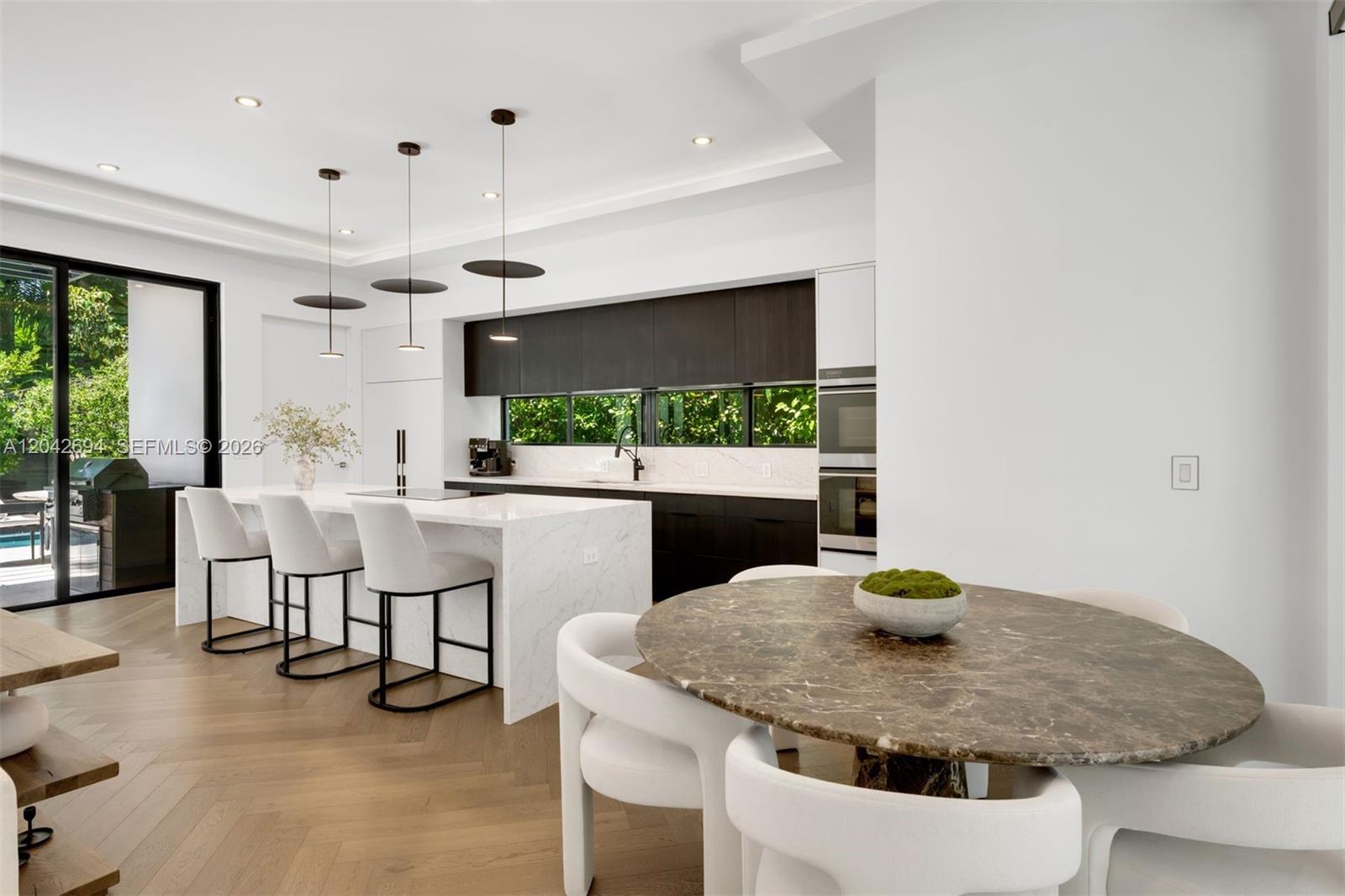 A modern kitchen features a marble island, dark cabinetry, and an adjacent circular dining table — 661 NE 120th St, Biscayne Park FL 33161, BISCAYNE PARK, FL
