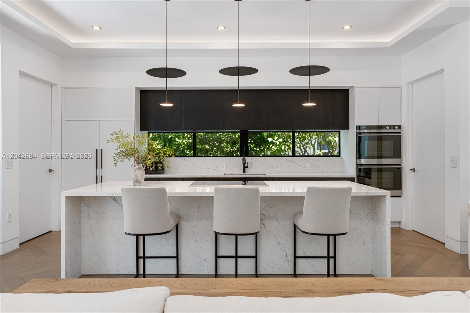 A modern kitchen features a marble waterfall island, three pendant lights, and dark cabinetry — 661 NE 120th St, Biscayne Park FL 33161, BISCAYNE PARK, FL