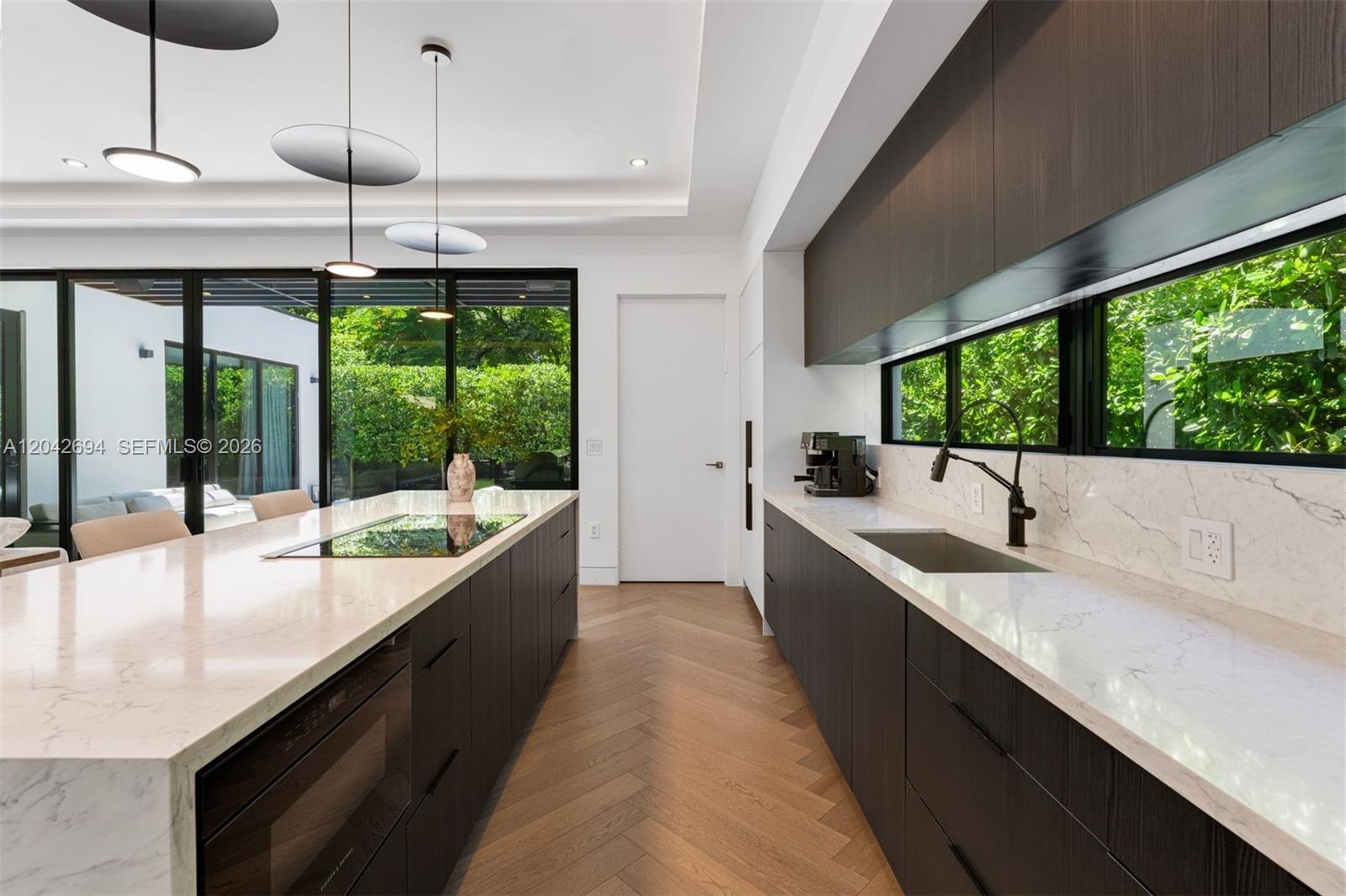 A modern kitchen features dark wood cabinetry, white marble countertops, and a herringbone wood floor — 661 NE 120th St, Biscayne Park FL 33161, BISCAYNE PARK, FL