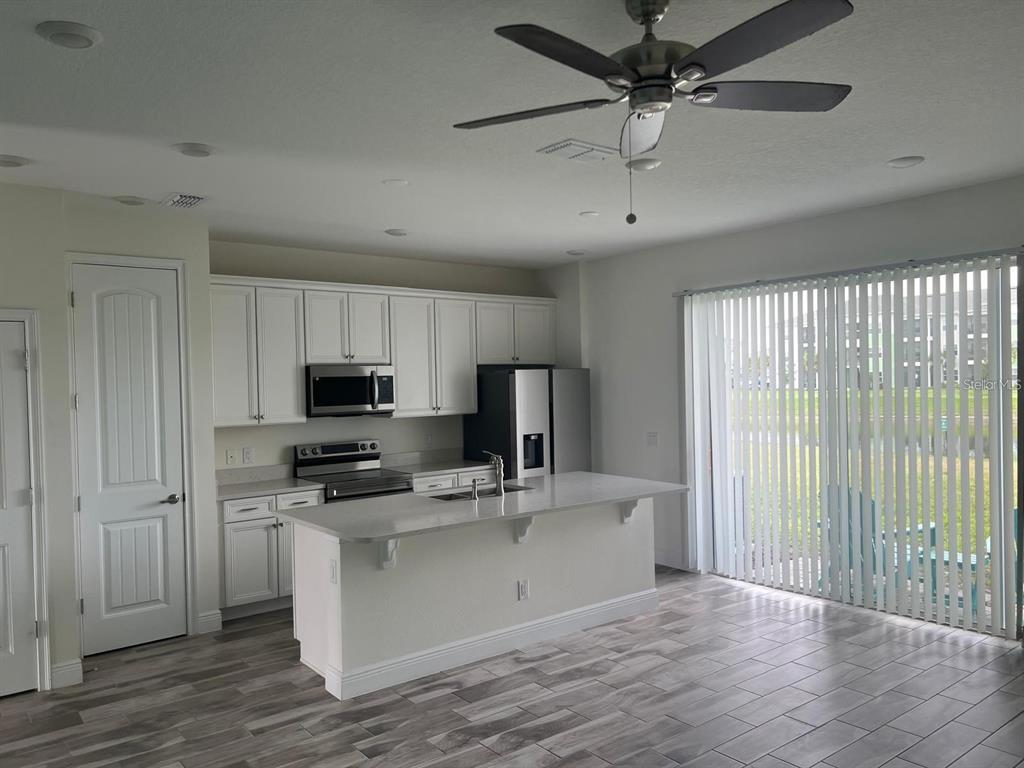 A kitchen with white cabinets, stainless steel appliances, a center island, and sliding glass doors — 3077 CARIBBEAN SOUL DRIVE, KISSIMMEE, FL