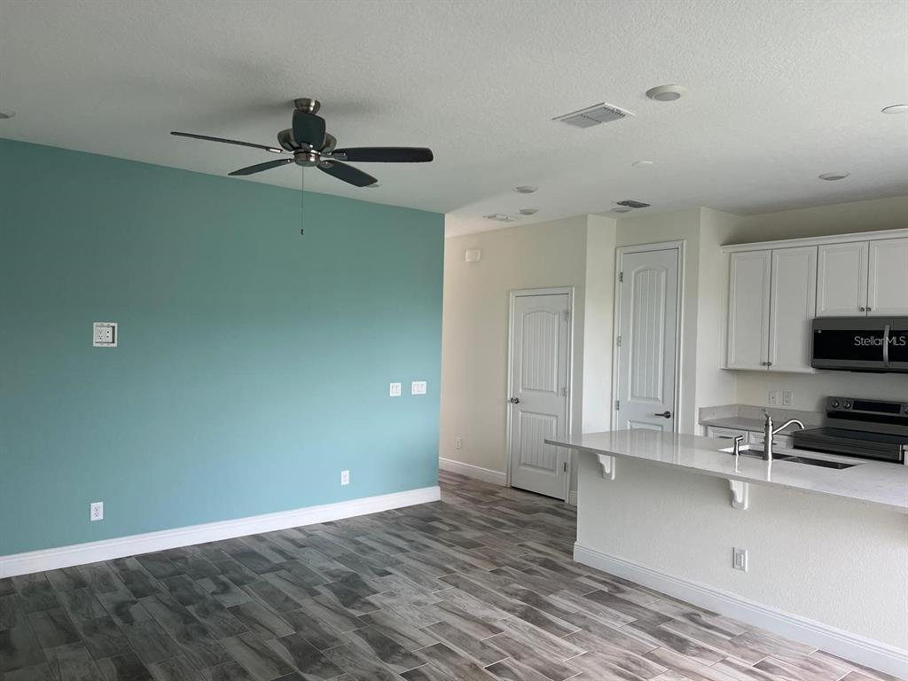 A kitchen with white cabinets and a breakfast bar opens to a teal-walled living area — 3077 CARIBBEAN SOUL DRIVE, KISSIMMEE, FL