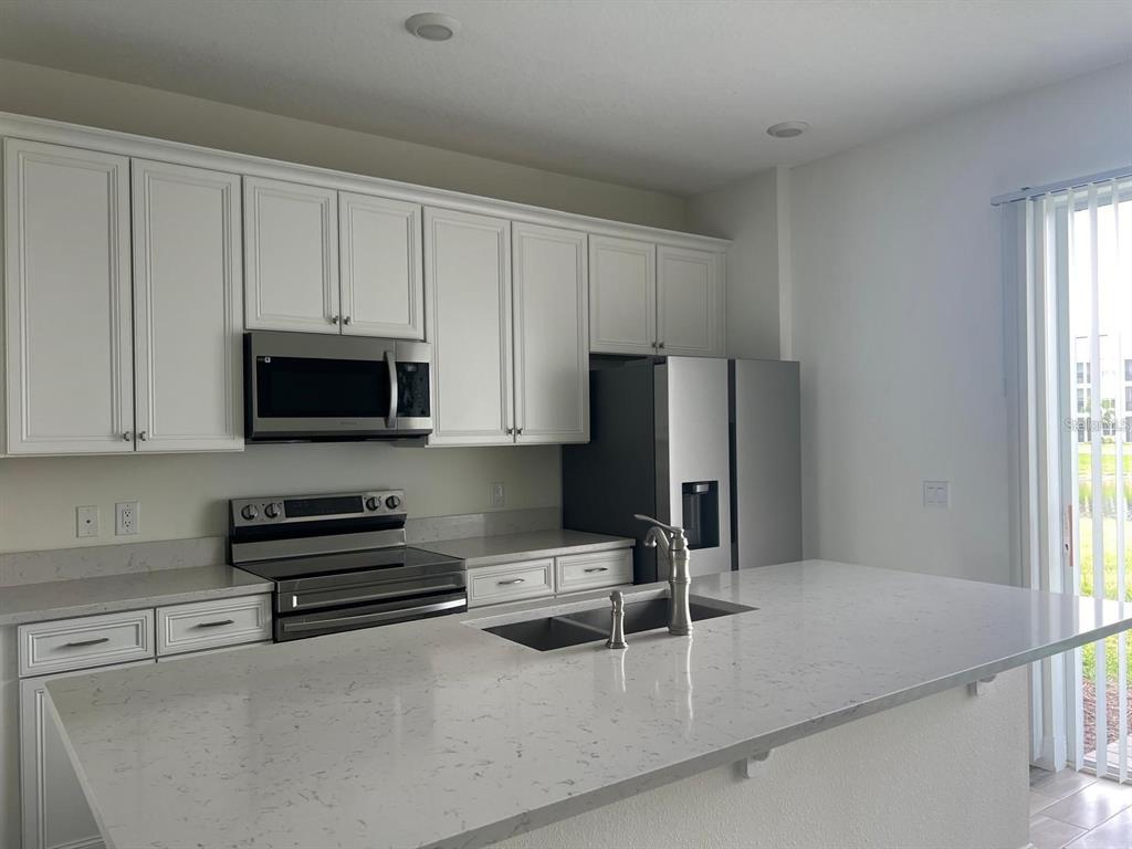 A kitchen features white cabinets, stainless steel appliances, and a large quartz-topped island — 3077 CARIBBEAN SOUL DRIVE, KISSIMMEE, FL