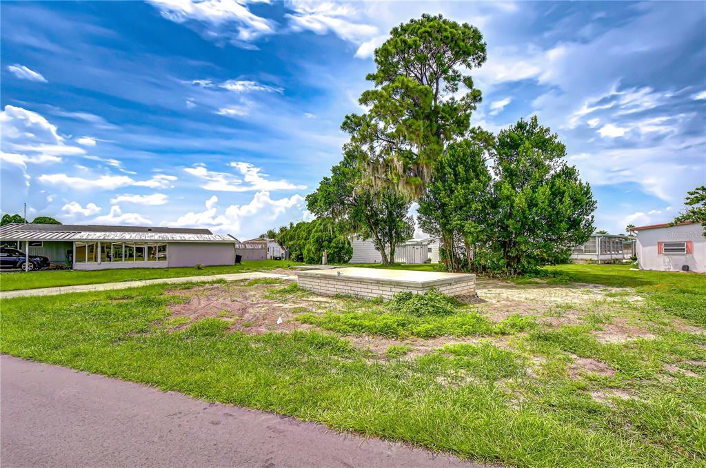 A vacant lot features a low brick structure, grass, and trees under a cloudy sky — 35127 ZEPHYR SHORES DRIVE, ZEPHYRHILLS, FL