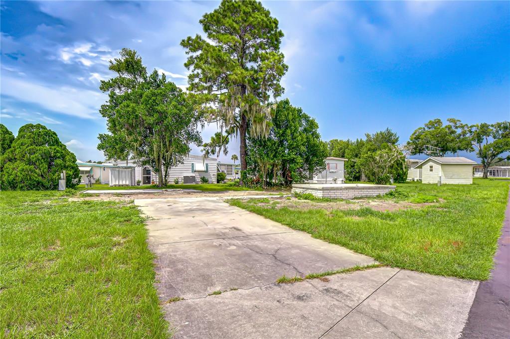 A concrete driveway leads to a vacant lot with trees and a small brick structure — 35127 ZEPHYR SHORES DRIVE, ZEPHYRHILLS, FL