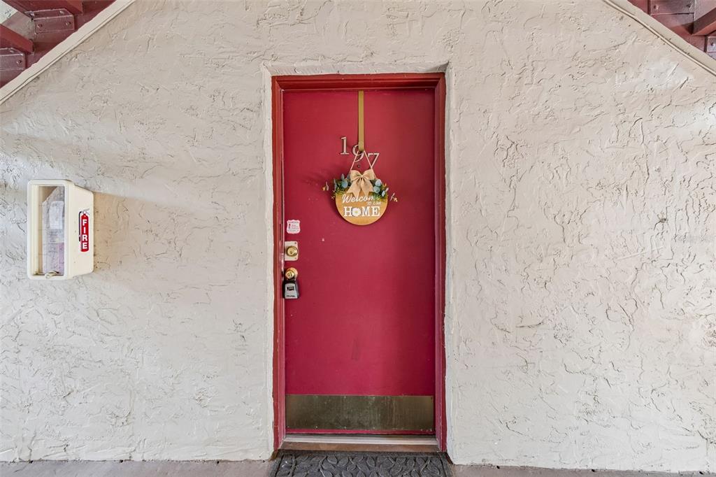 A red front door with a welcome wreath is set into a textured stucco wall — 3841 S LAKE DRIVE UNIT 197, TAMPA, FL