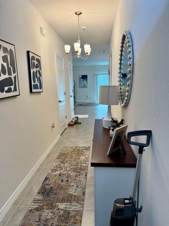 A hallway features a chandelier, a runner rug, a console table, and wall art — 2372 PENGUIN BLVD, DAVENPORT, FL