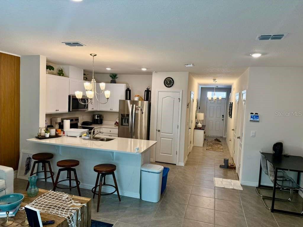 A kitchen with white cabinets, a quartz island, and bar seating overlooks a tiled hallway — 2372 PENGUIN BLVD, DAVENPORT, FL
