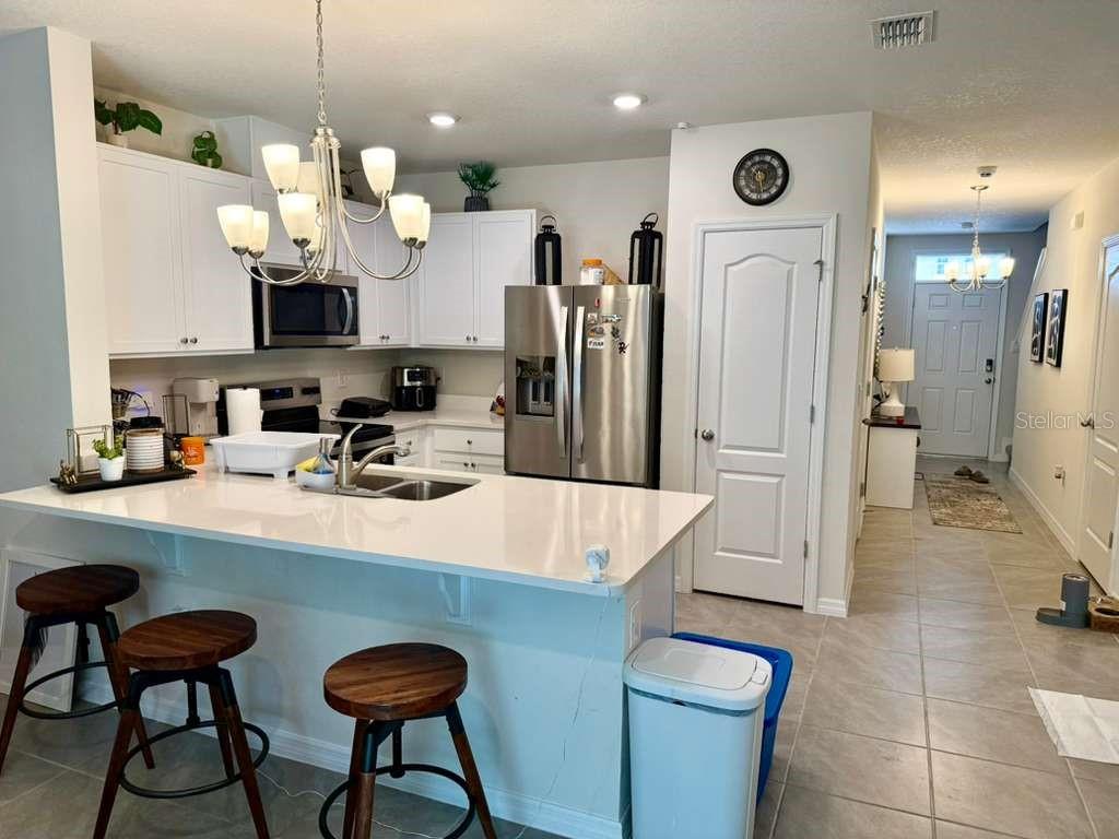 A kitchen features white cabinets, stainless steel appliances, a quartz island, and bar stools — 2372 PENGUIN BLVD, DAVENPORT, FL