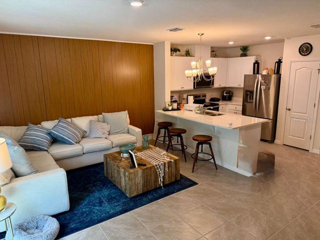 A living room with wood-paneled walls opens to a kitchen featuring white cabinets and island — 2372 PENGUIN BLVD, DAVENPORT, FL