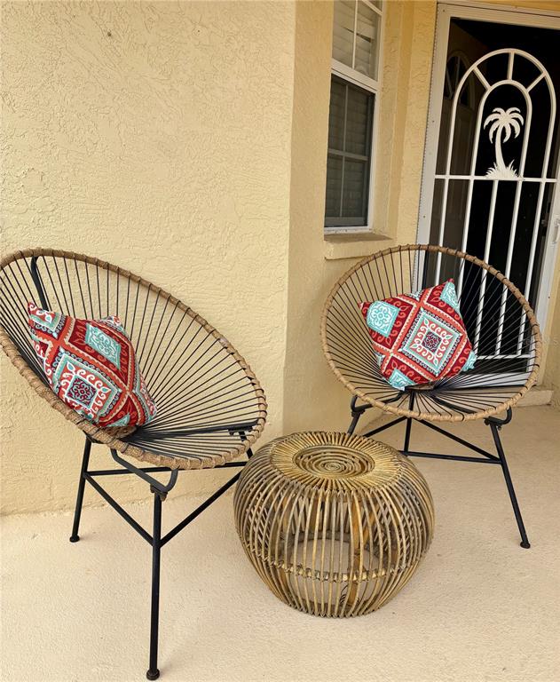 Two round wicker chairs with patterned pillows and a matching side table sit outdoors — 703 CASA DEL LAGO WAY UNIT 703, VENICE, FL