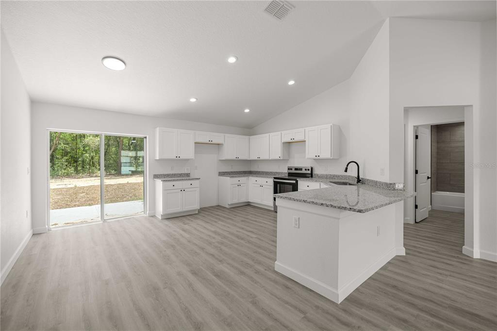 A bright kitchen features white cabinets, granite countertops, and light wood-look flooring — 22930 SW MARINE BOULEVARD, DUNNELLON, FL