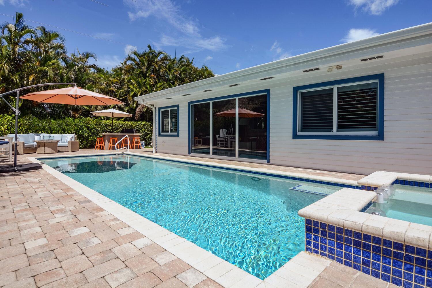 A backyard swimming pool and hot tub sit beside a white house with blue trim — 3396 Pebble Place, Jupiter FL 33469, JUPITER, FL