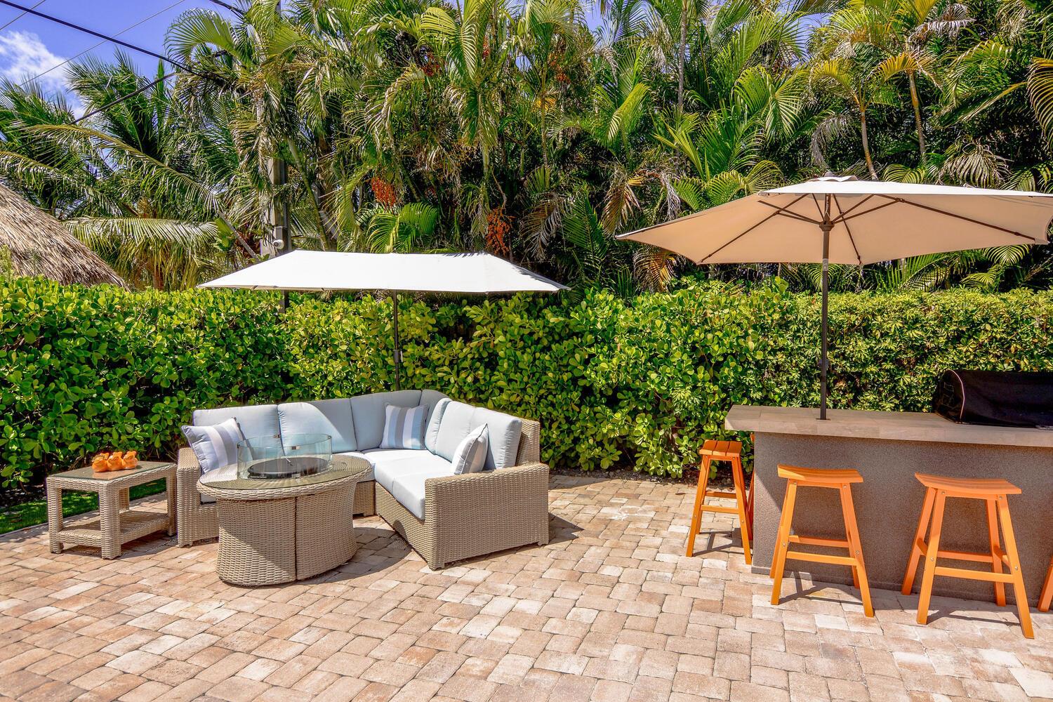 An outdoor patio features a wicker sectional, fire pit, bar stools, and two umbrellas — 3396 Pebble Place, Jupiter FL 33469, JUPITER, FL