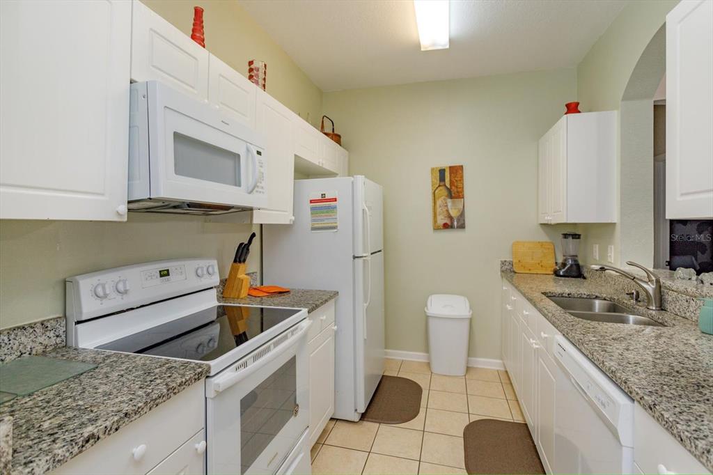 A kitchen features white cabinets, granite countertops, white appliances, and light-colored tile flooring — 2310 SILVER PALM DR UNIT 104, KISSIMMEE, FL
