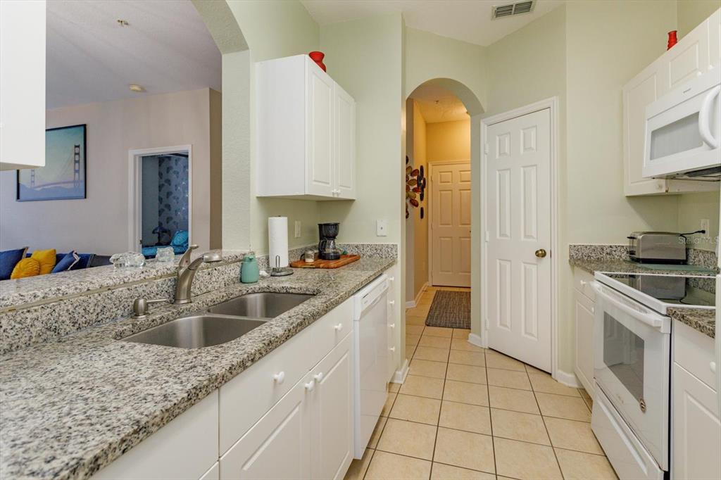 A kitchen features white cabinets, granite countertops, a double sink, and white appliances — 2310 SILVER PALM DR UNIT 104, KISSIMMEE, FL