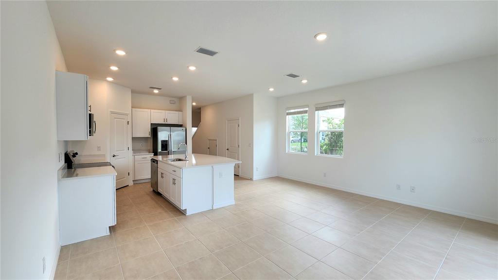 A bright kitchen with white cabinets and a center island opens to a tiled living area — 16656 BERGAMO PLACE, LAKEWOOD RANCH, FL