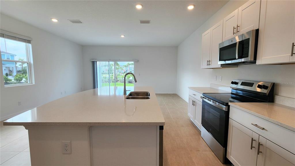 A kitchen features a large quartz island, white cabinetry, and stainless steel appliances — 16656 BERGAMO PLACE, LAKEWOOD RANCH, FL