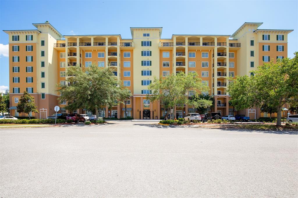 A multi-story yellow and tan apartment building stands behind a large paved parking lot — 8100 POINCIANA BOULEVARD UNIT 2312, ORLANDO, FL
