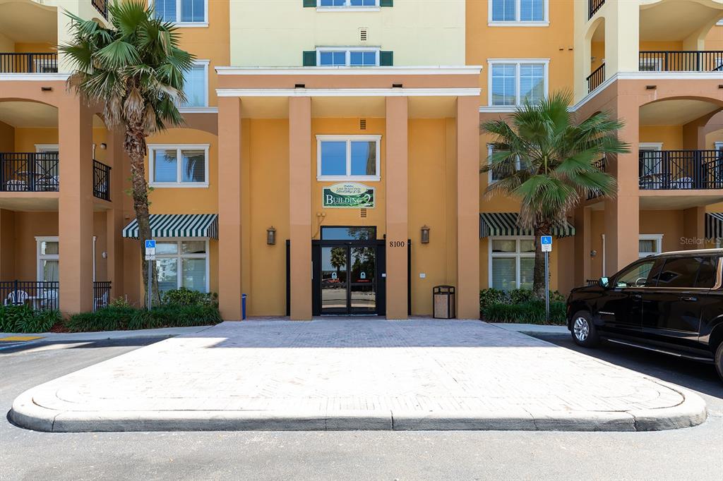 The exterior entrance of a multi-story apartment building features a paved driveway and palm trees — 8100 POINCIANA BOULEVARD UNIT 2312, ORLANDO, FL