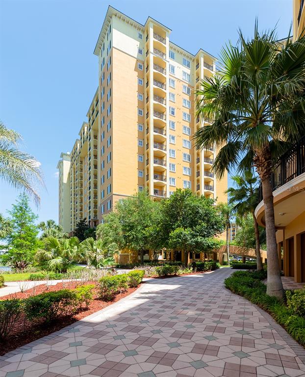 A tall, yellow multi-story apartment building stands above a paved walkway and palm trees — 8100 POINCIANA BOULEVARD UNIT 2312, ORLANDO, FL